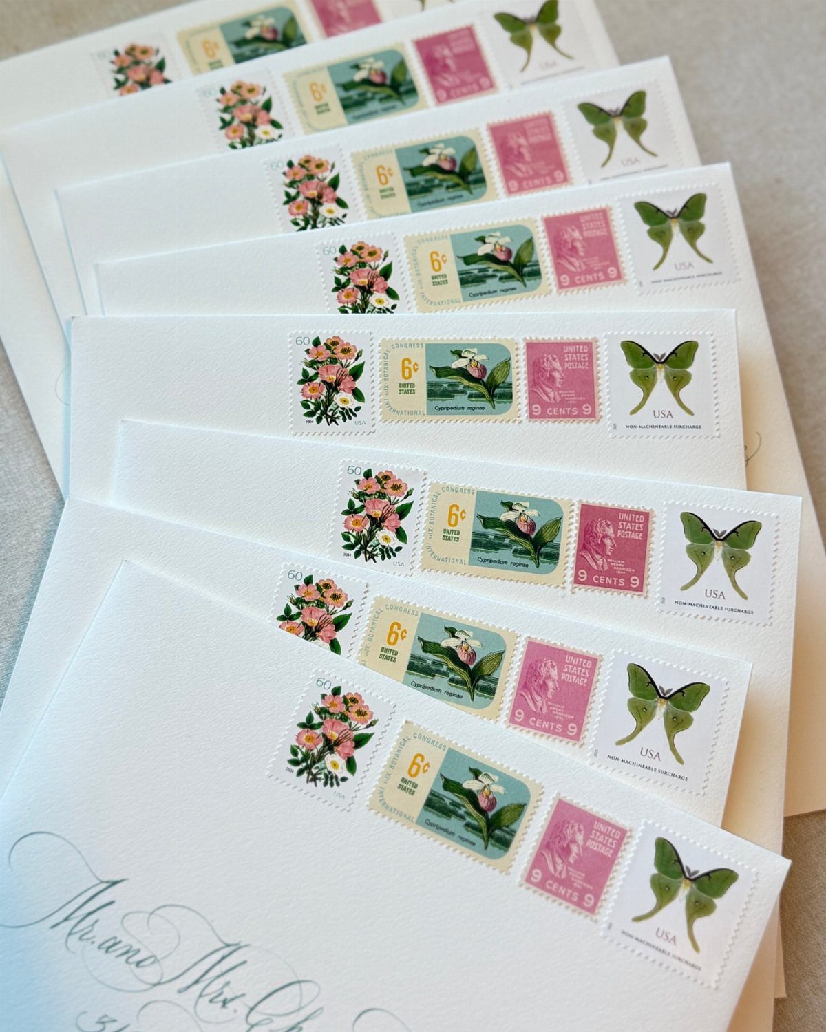 White envelopes with vintage floral and butterfly postage stamps arranged in a stack.