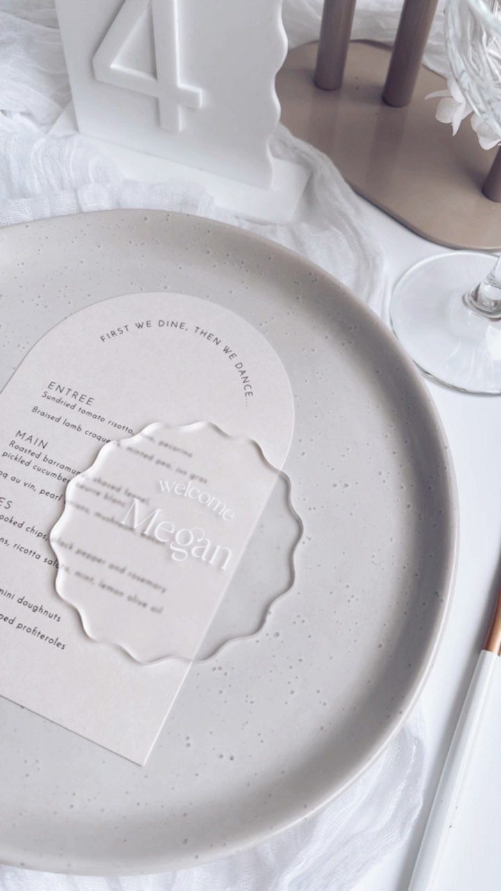 Scalloped acrylic place card with name Megan on a grey ceramic plate