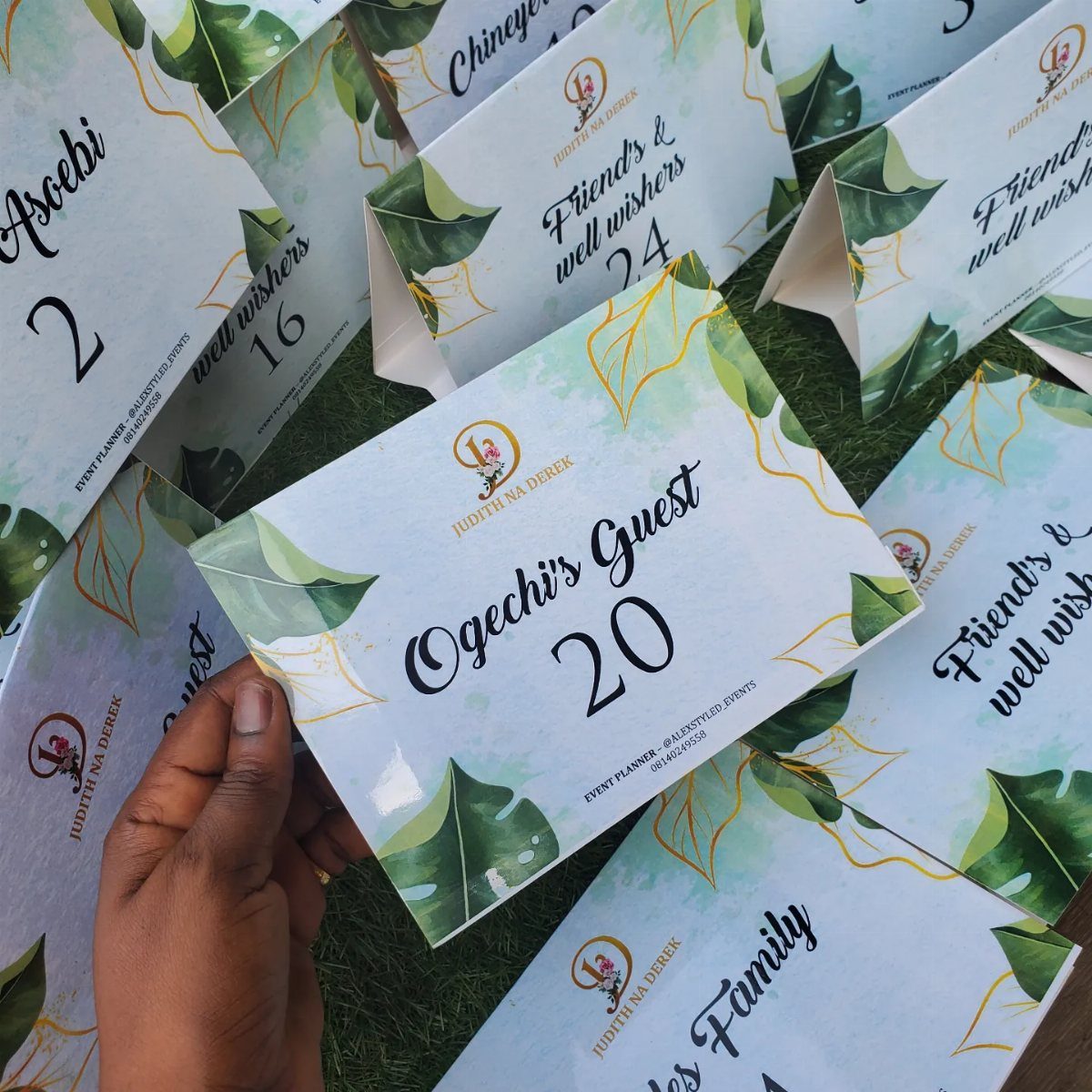 White wedding table cards with green leaf designs and guest names on grass