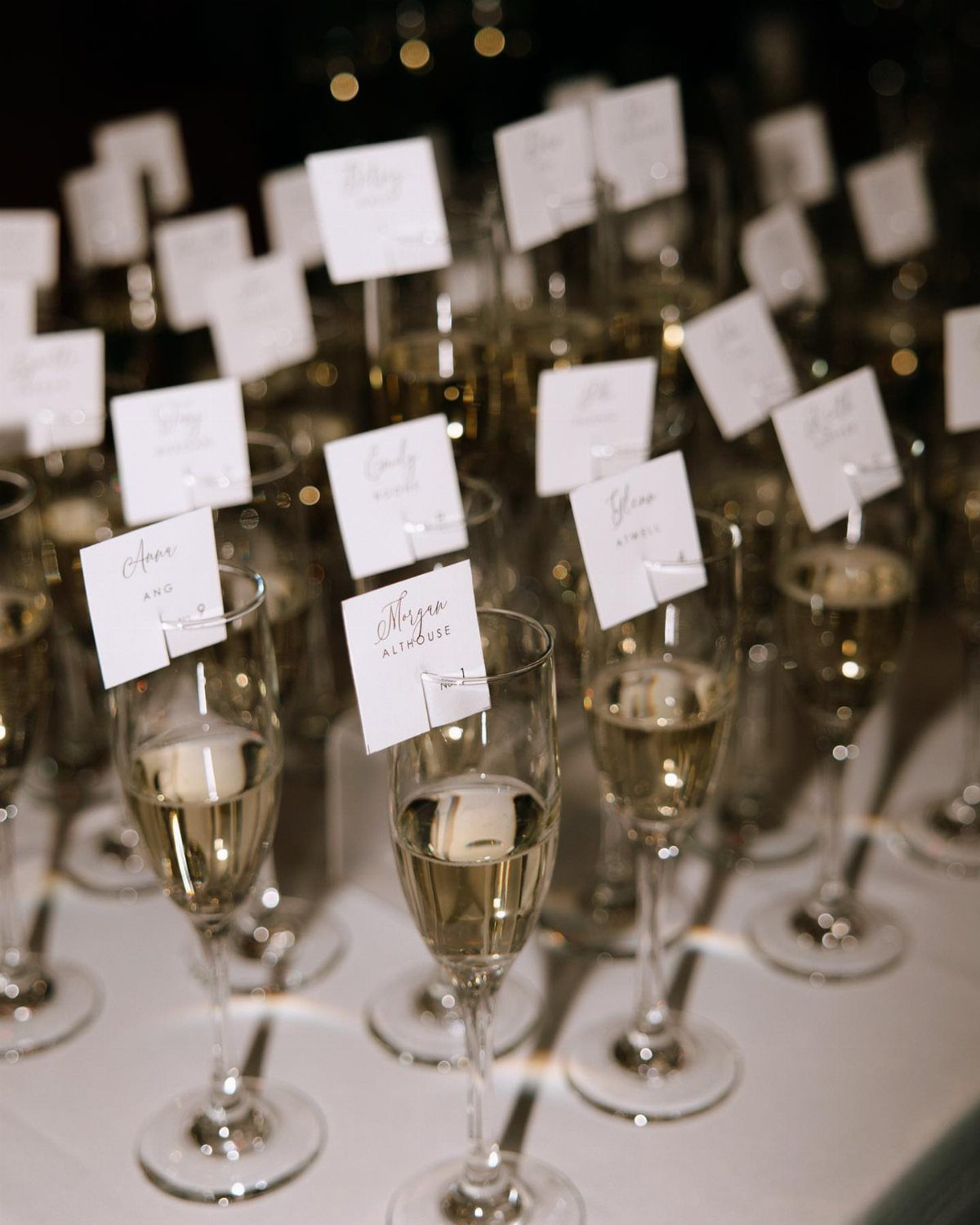 Champagne flutes with white name cards clipped to the rims on a table.