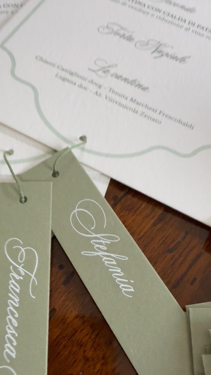 Sage green paper name tags with white calligraphy on a wooden table.