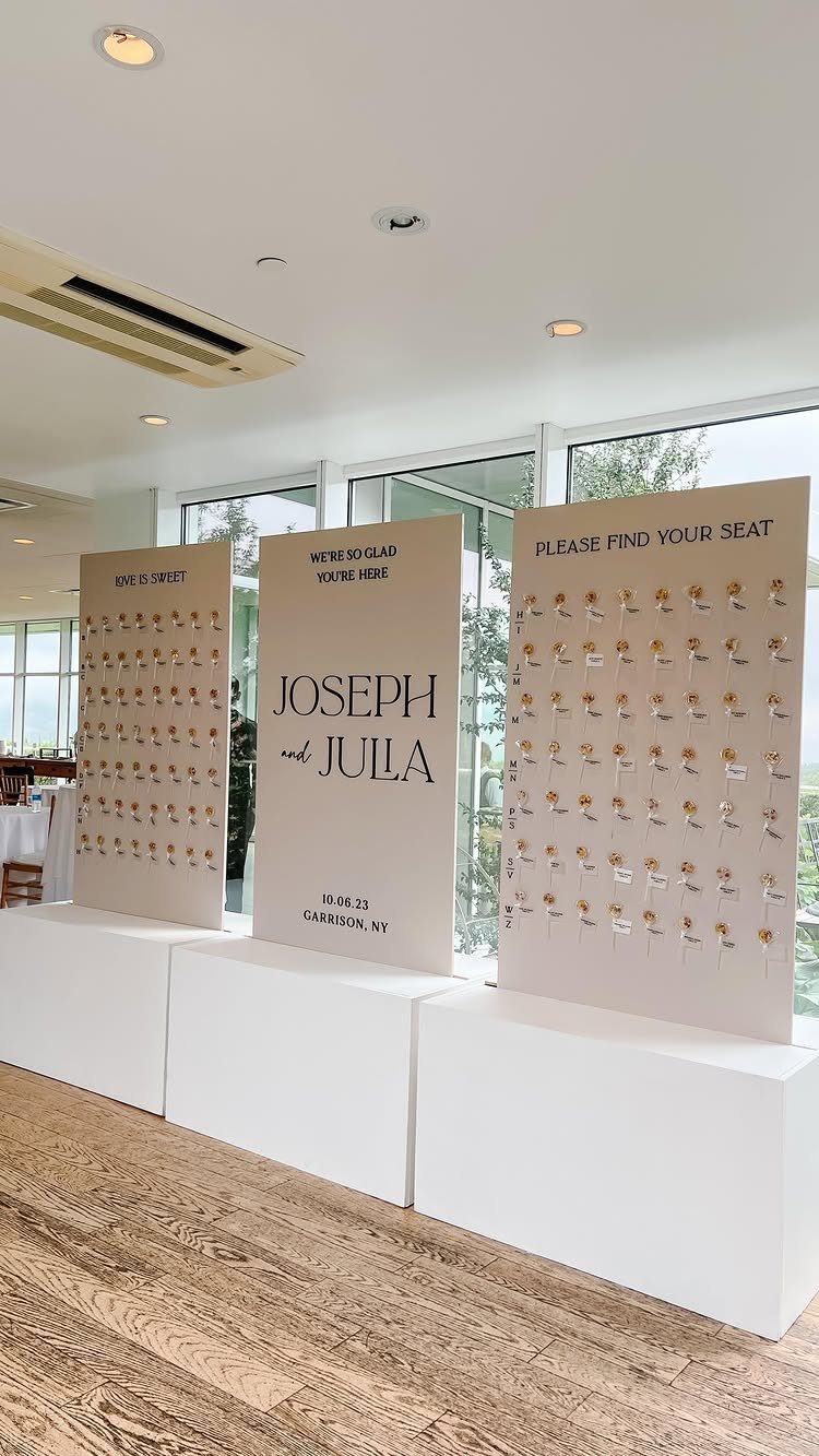Lollipop table number wall display with name tags on beige panels for a wedding.