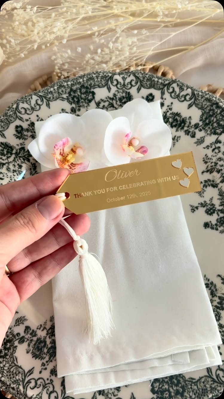 Gold metallic name tag with white tassel on a white napkin and orchids