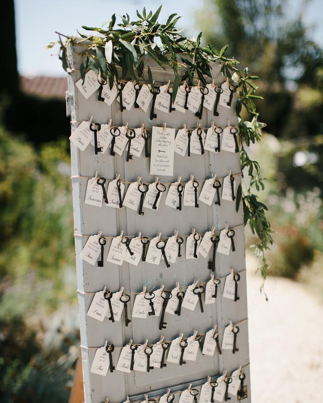 Vintage metal keys with white name tags hanging on a white wooden board.