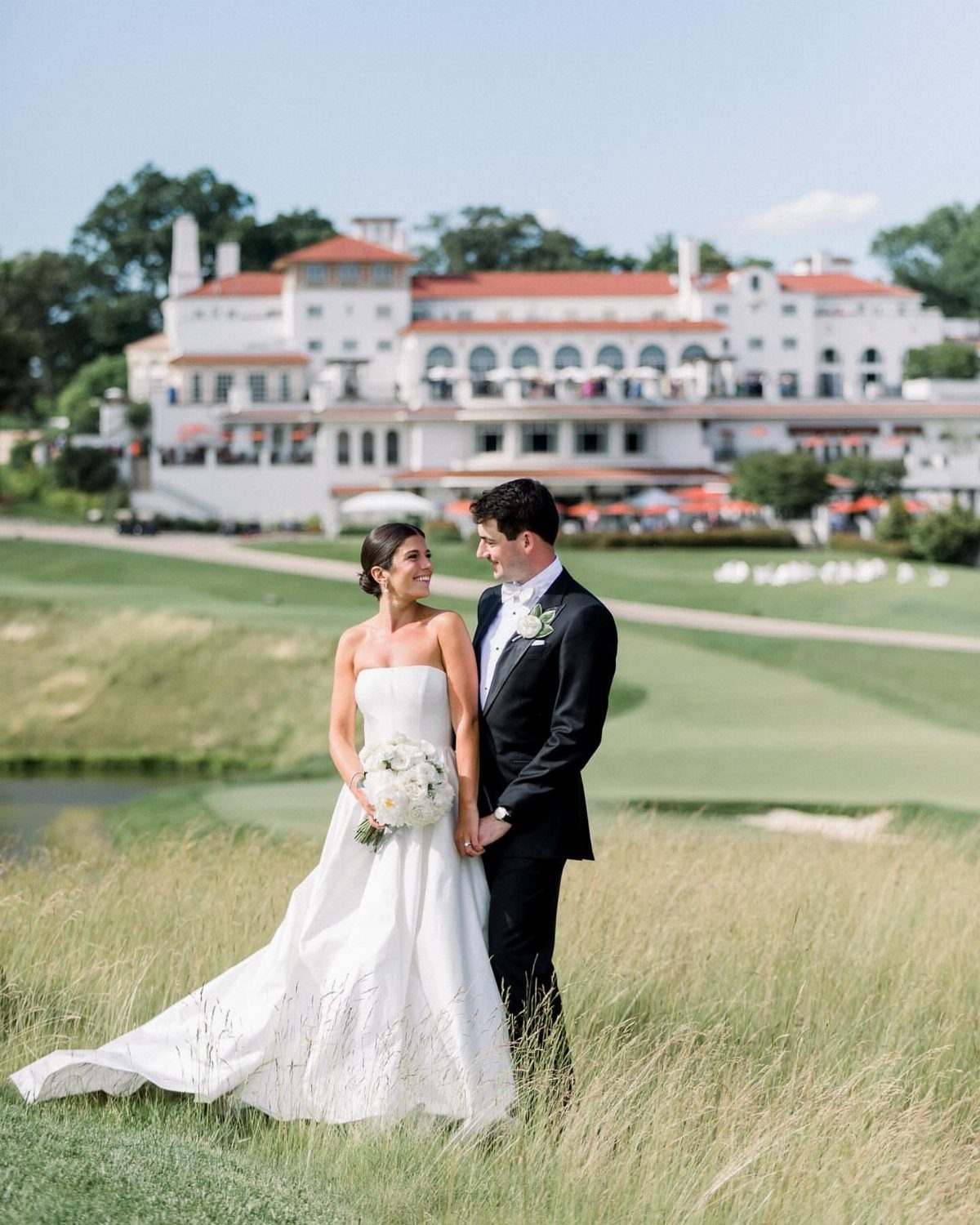 Bride and groom holding hands in a field before a white clubhouse