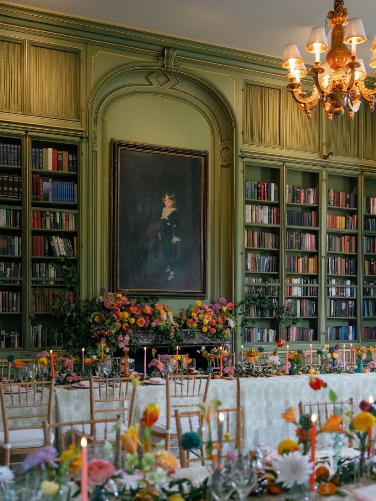 Elegant dining table with colorful flowers in a green library with a portrait.