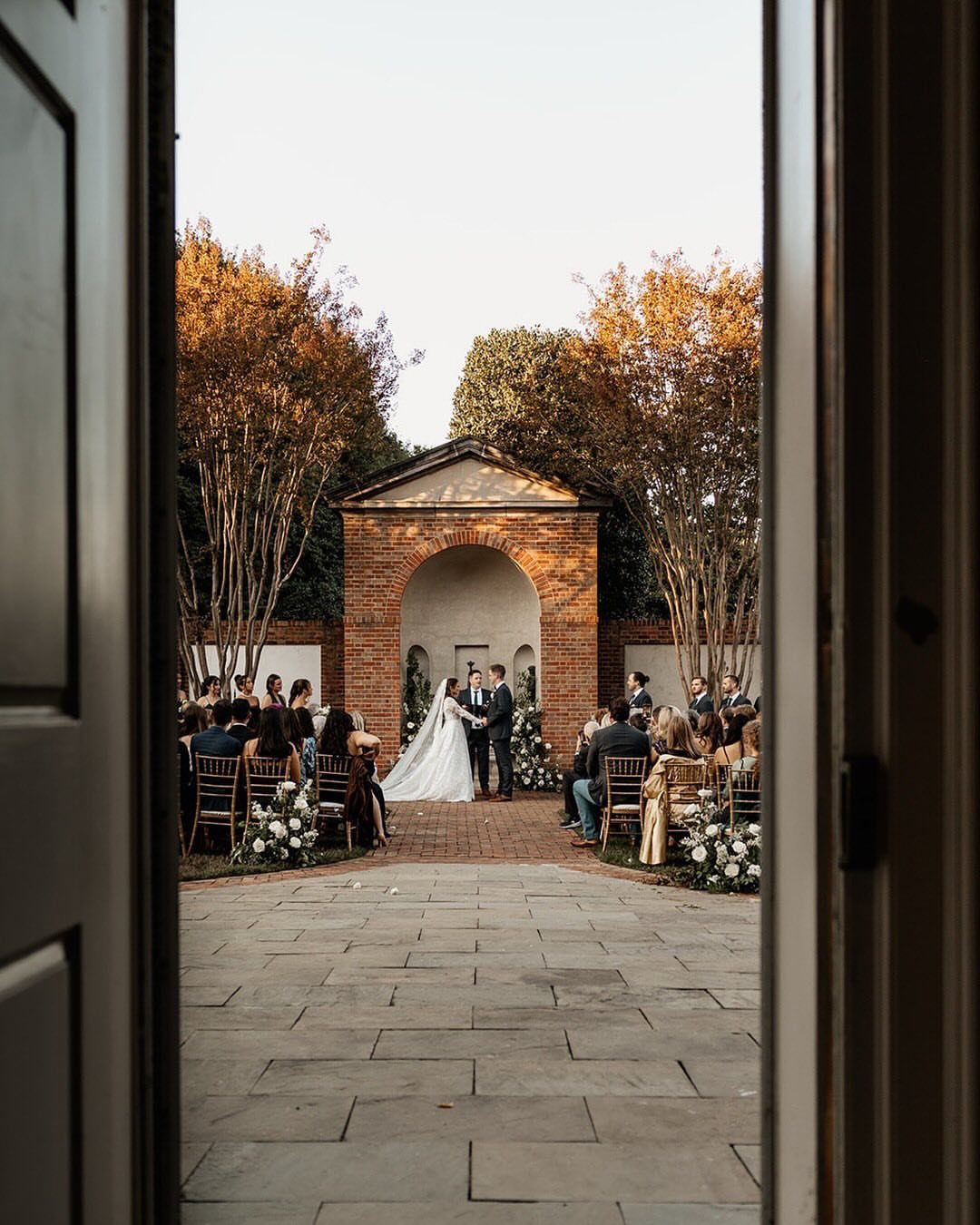 Bride and groom during an outdoor wedding ceremony in a brick courtyard garden.