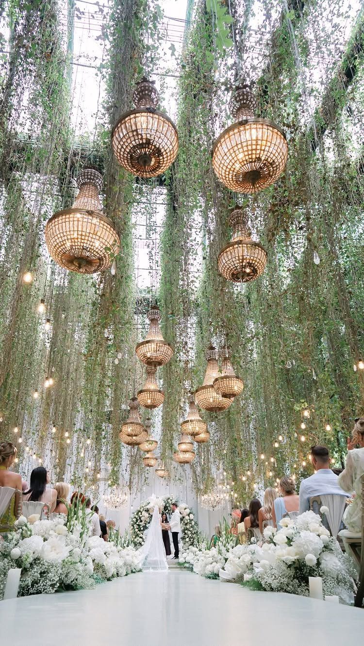 Lavish wedding venue in a glass conservatory with hanging greenery and gold chandeliers.
