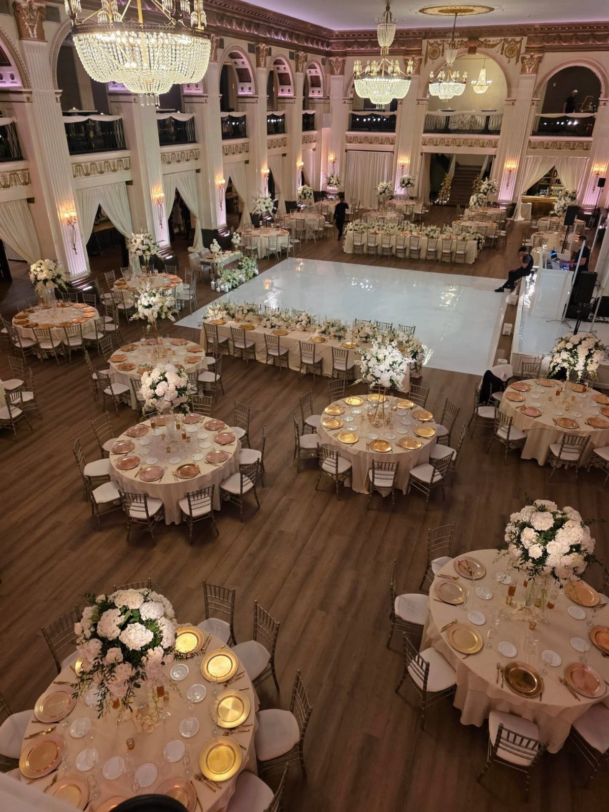 Opulent ballroom with round tables, white floral centerpieces, and large crystal chandeliers.