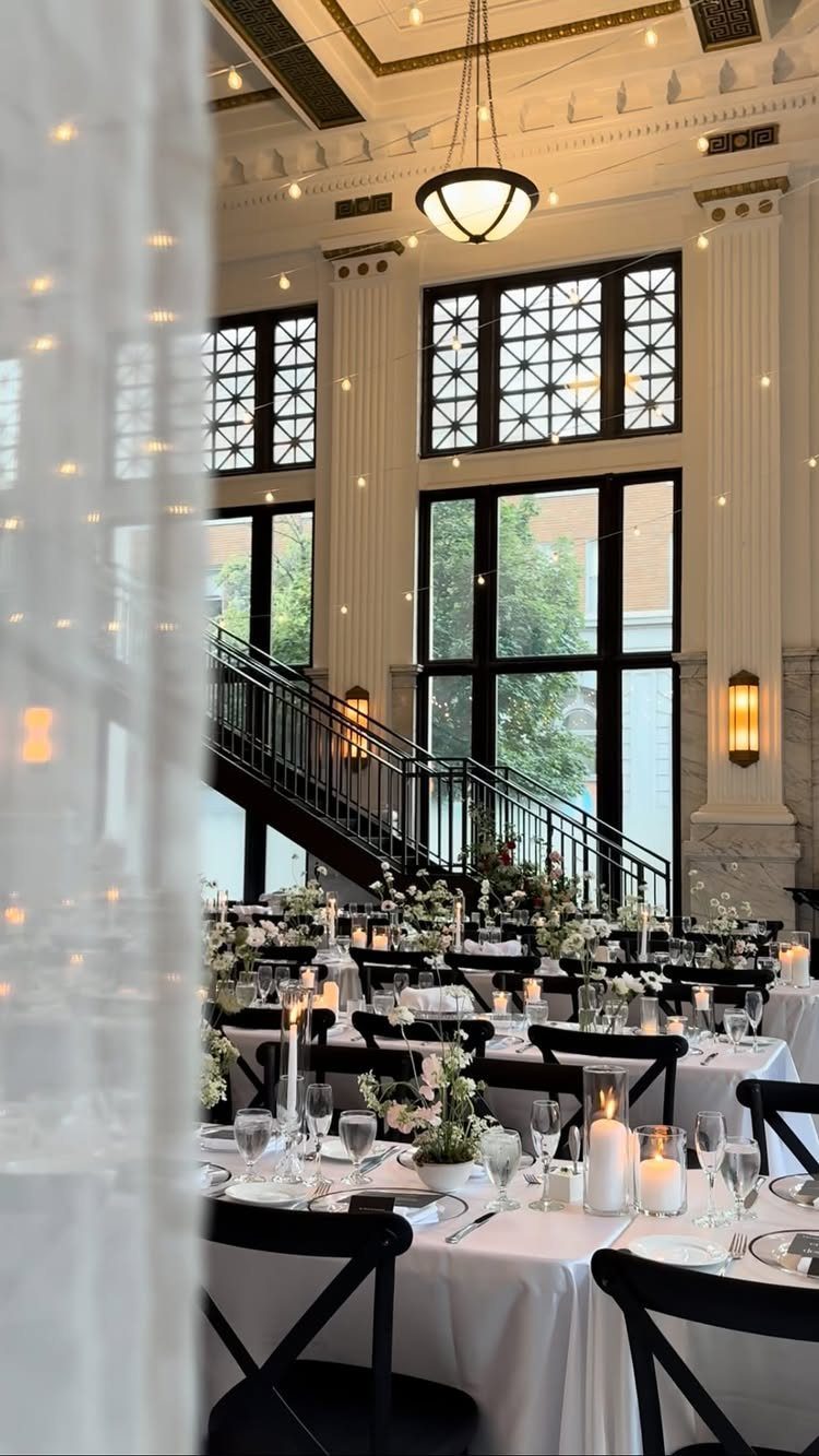 Elegant wedding reception venue with white tables, black chairs, and large windows.