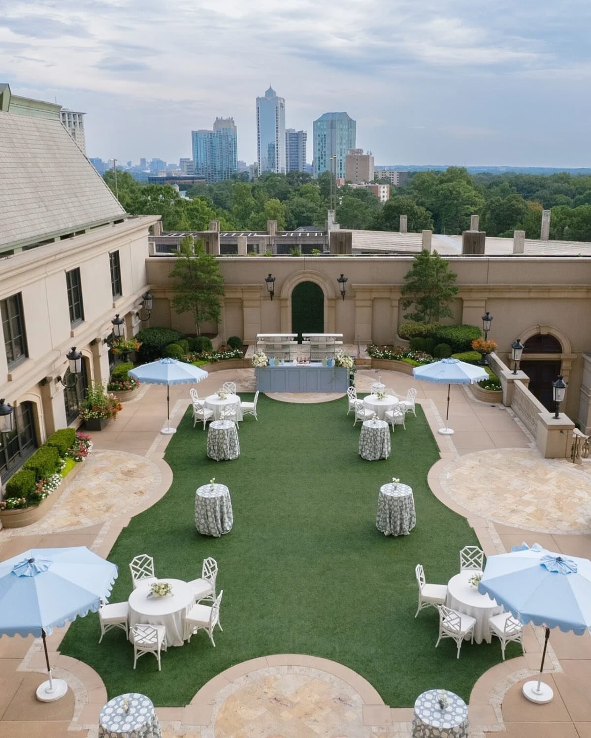 Outdoor terrace with white tables, blue umbrellas, and a city skyline background.