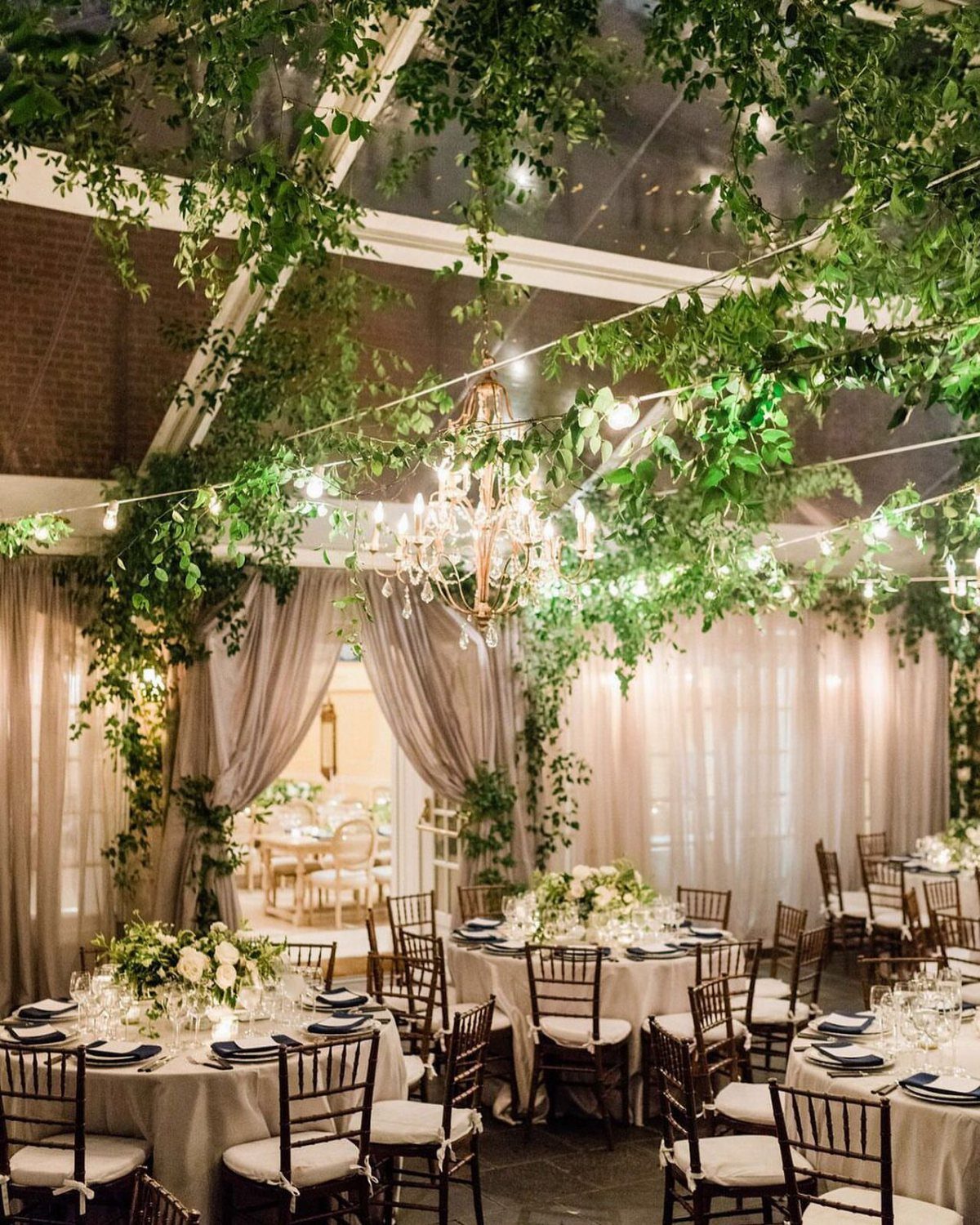 Wedding reception tables under a ceiling of green vines and crystal chandeliers