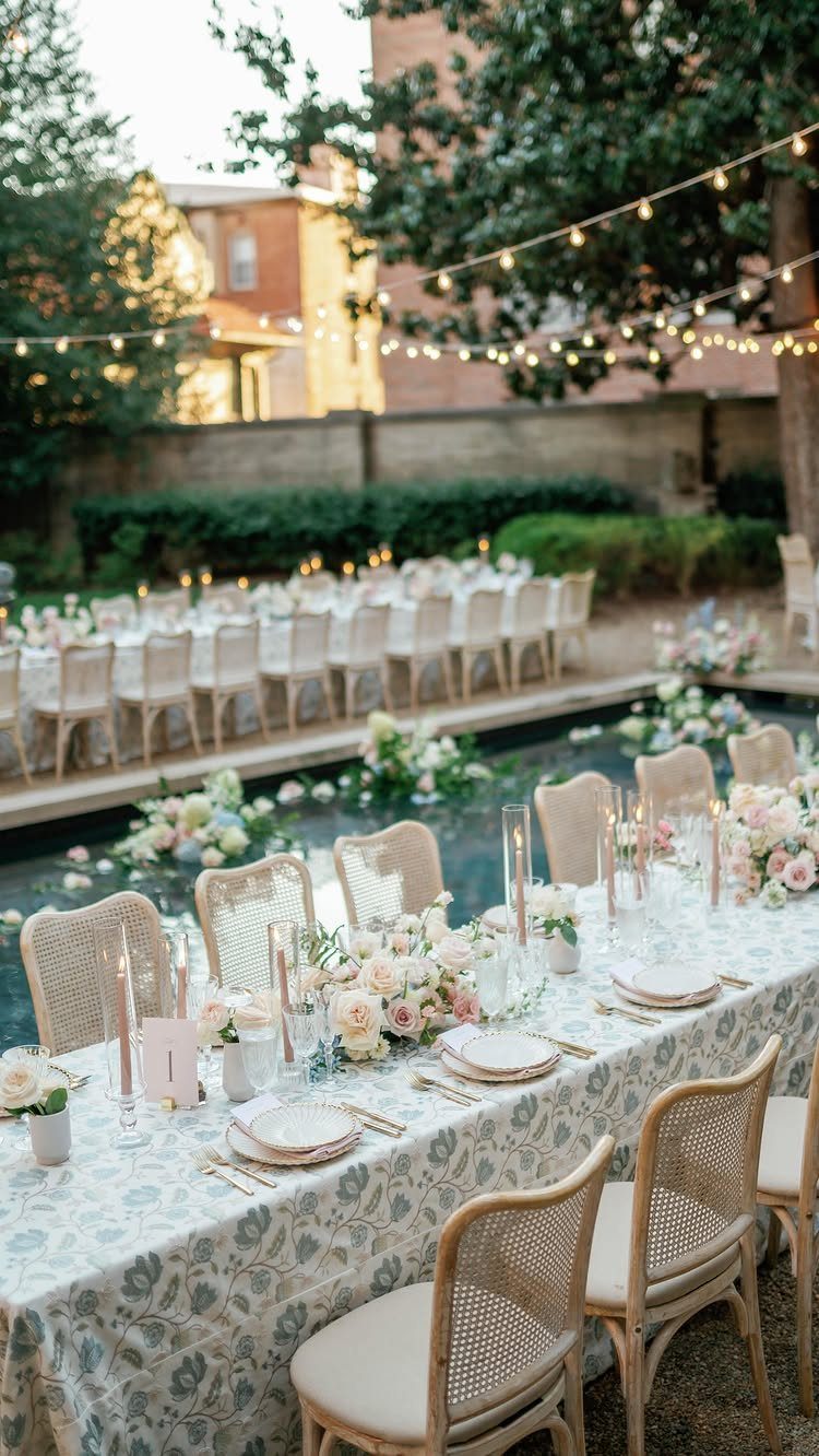 Outdoor wedding reception table with floral linens and candles next to a pool.