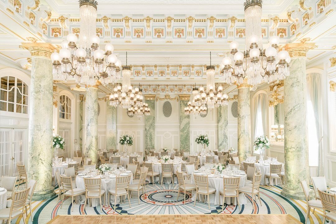 Opulent ballroom with crystal chandeliers, marble columns, and set dining tables for weddings.