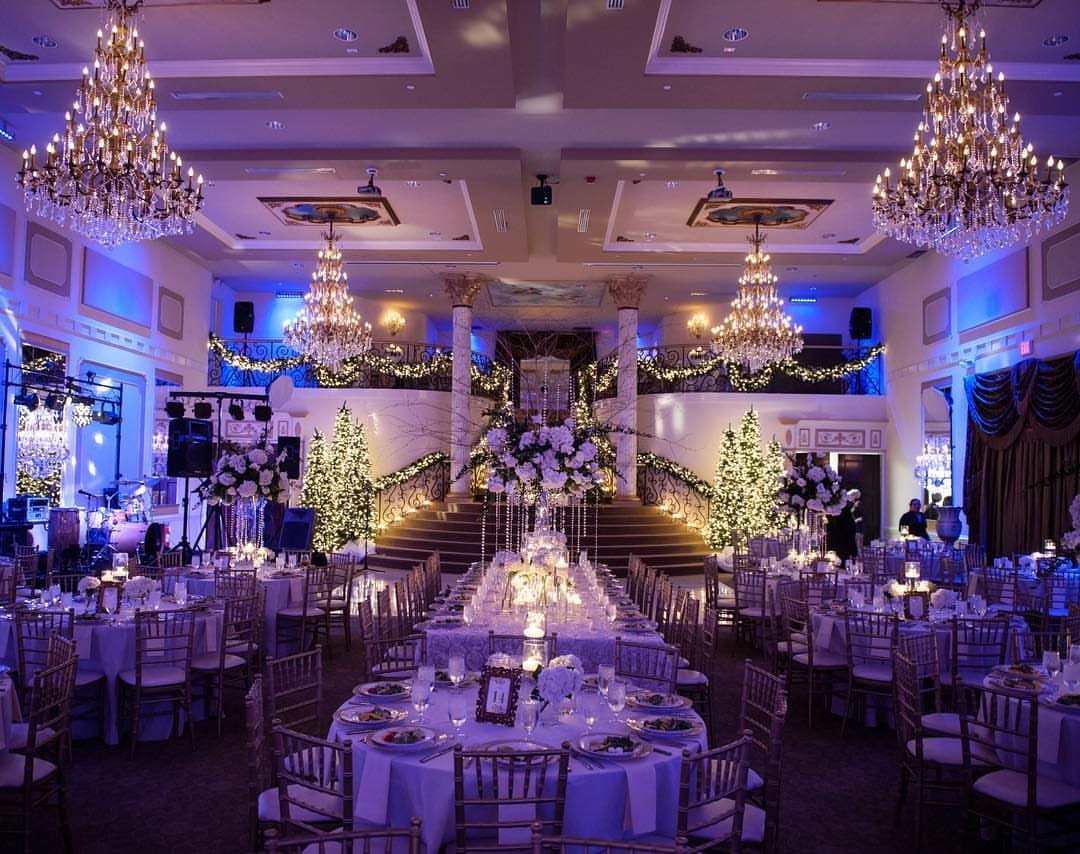 Lavish ballroom with set tables and a grand staircase decorated with greenery.