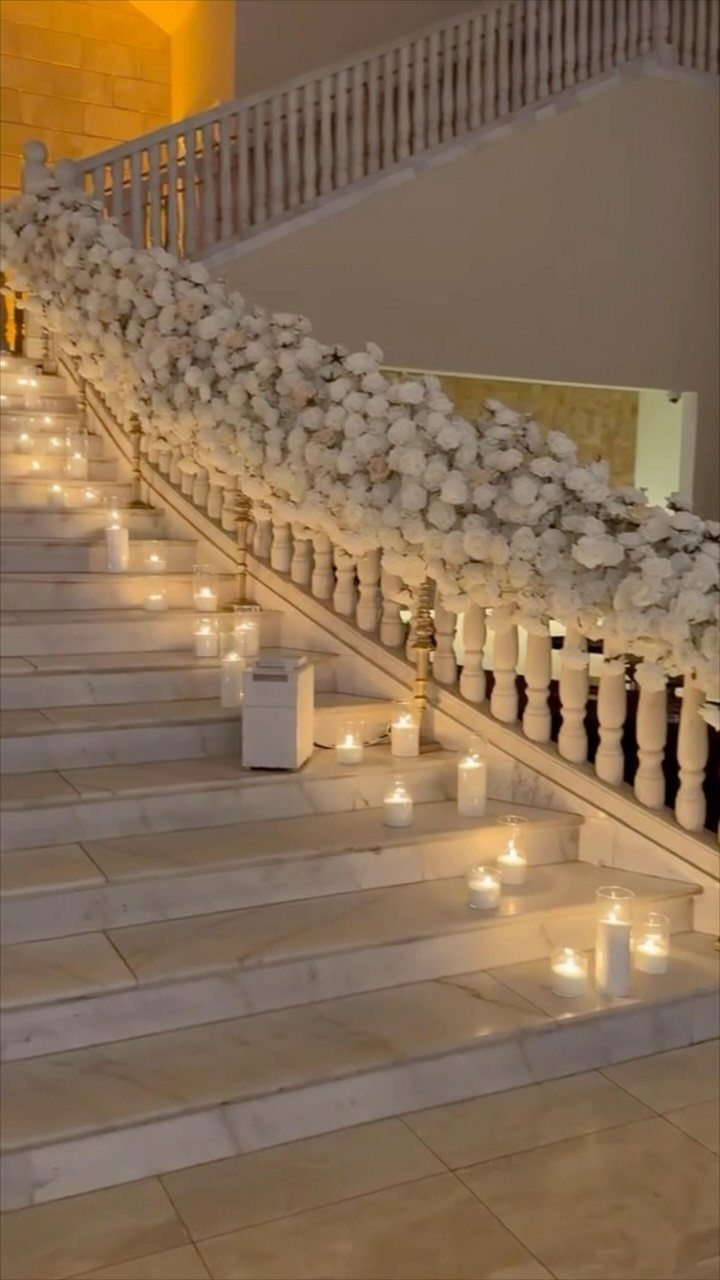 White marble staircase decorated with white floral garlands and glowing white candles.