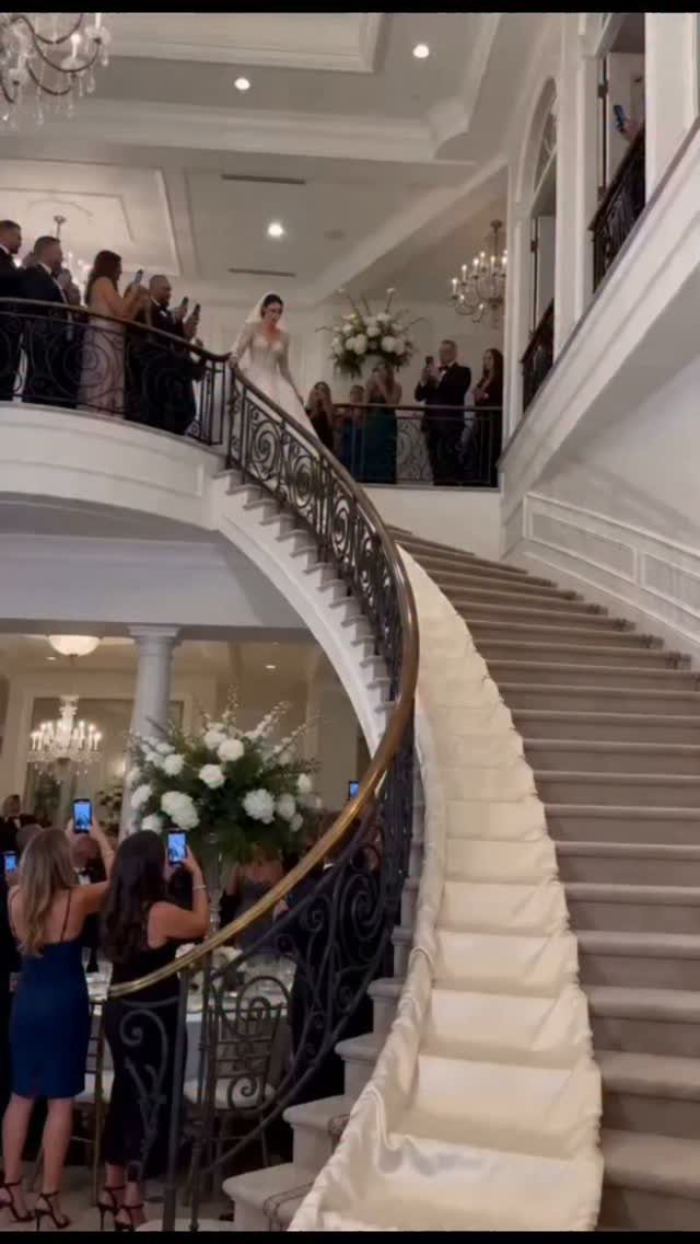 Bride in white gown descending a grand curved staircase at a wedding venue