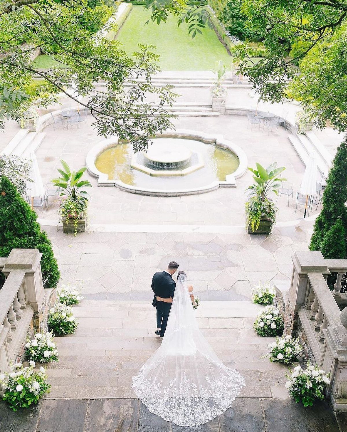 Bride and groom standing on a stone staircase overlooking a courtyard fountain