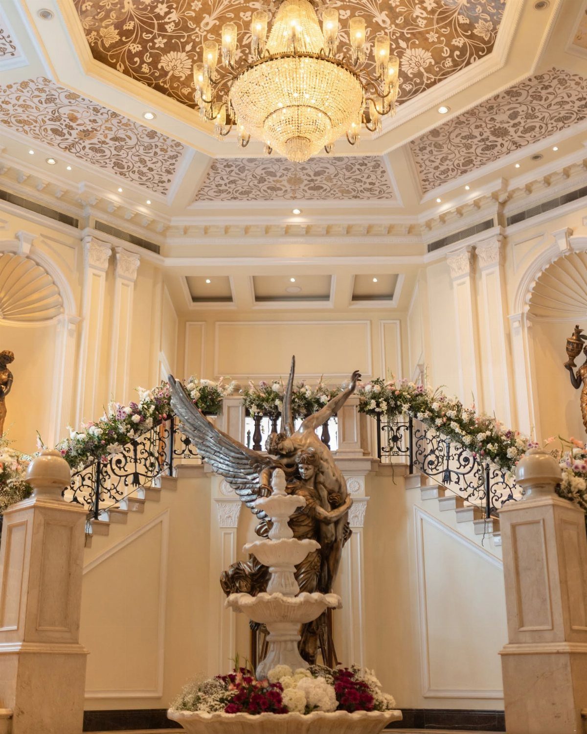Ornate white staircase with floral decorations, a tiered fountain, and a crystal chandelier.
