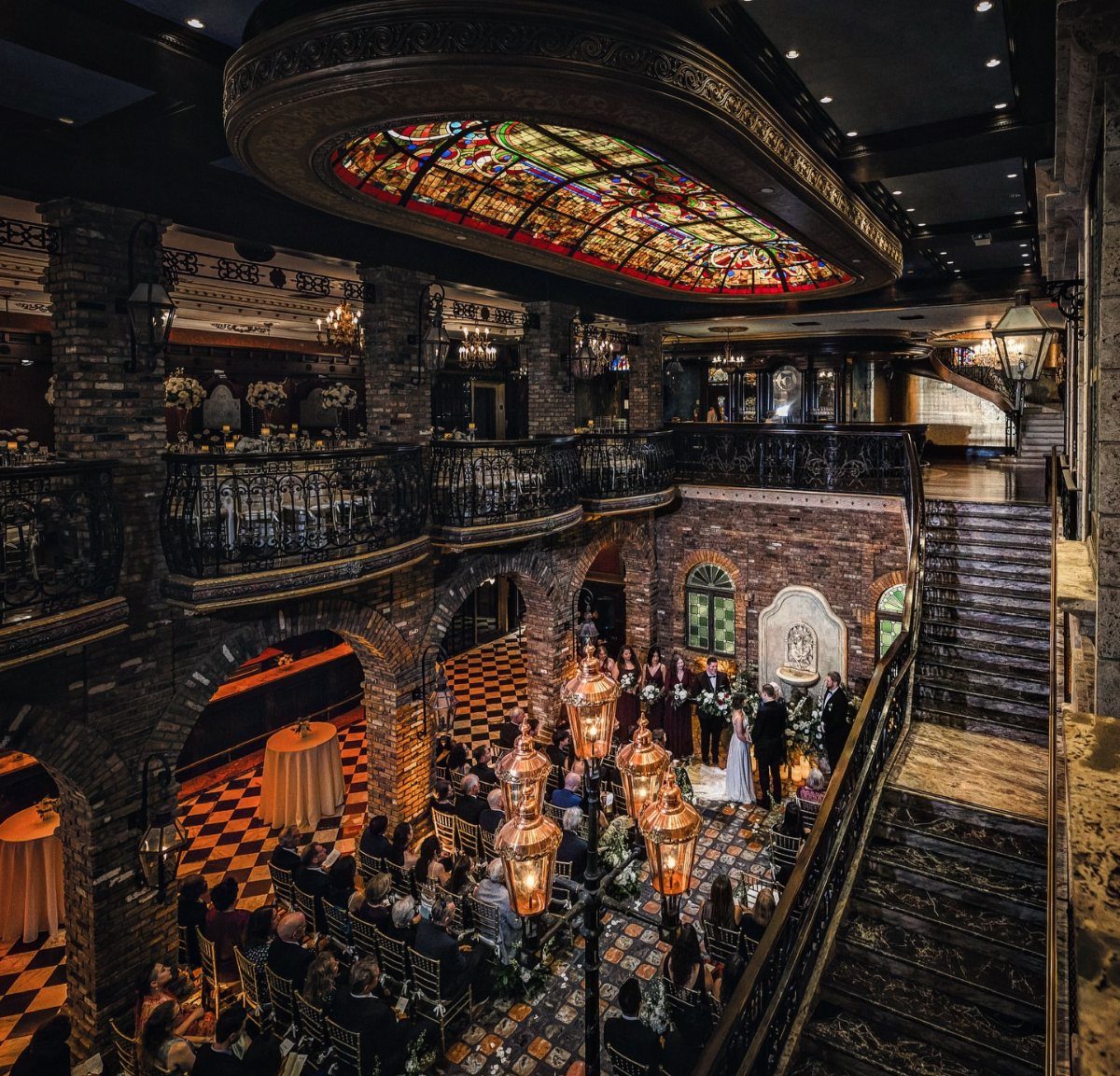 Ornate indoor venue with stained glass ceiling, brick walls, and a grand staircase.