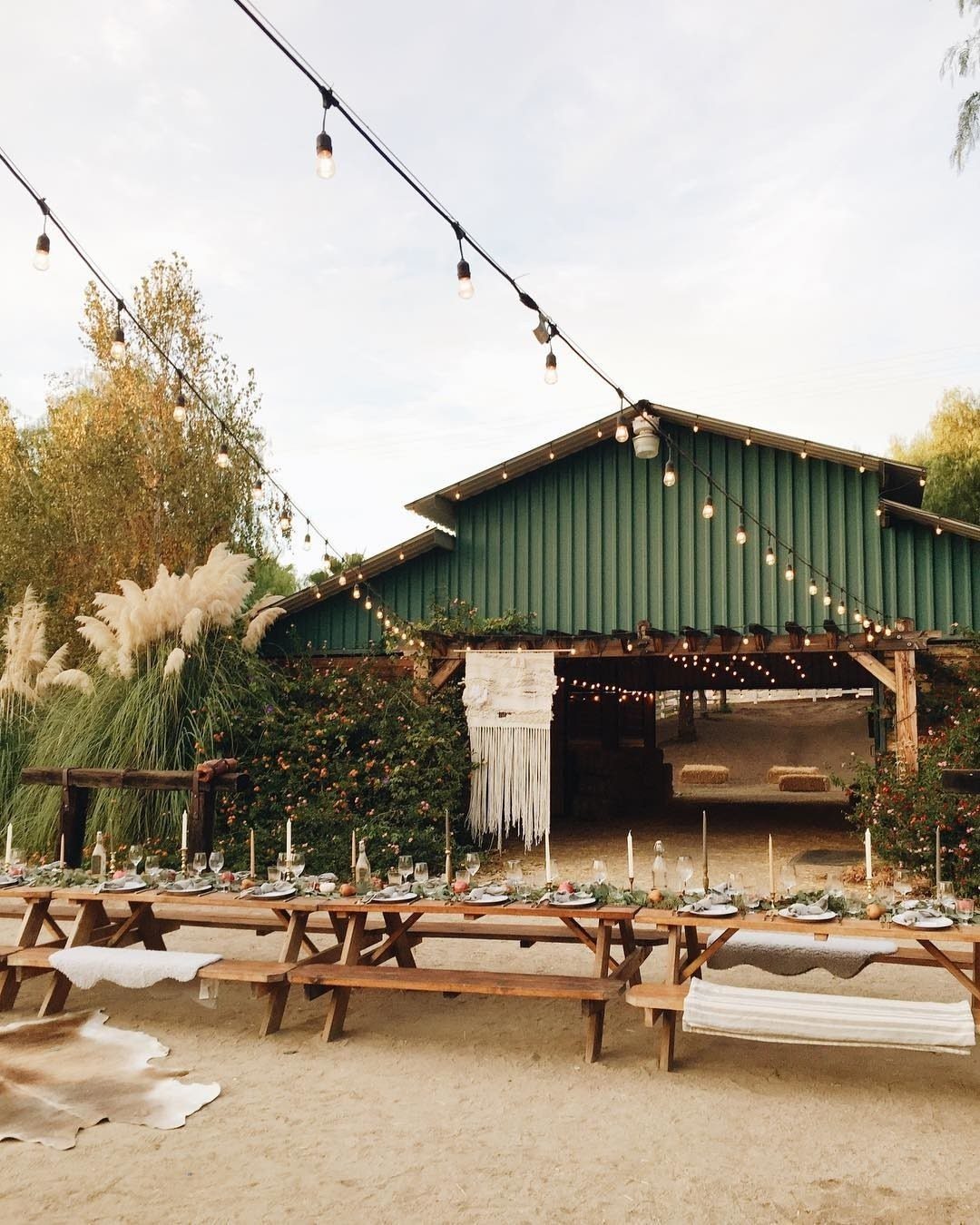 Green wooden barn venue with a long decorated banquet table and overhead string lights.