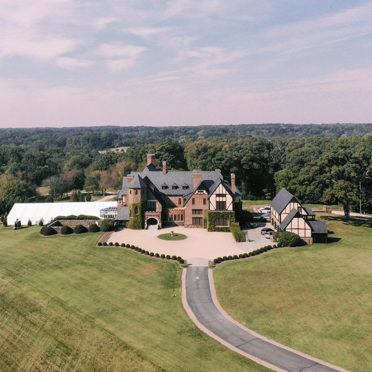 Grand English Tudor estate with half-timbered architecture, gravel driveway, and white event tent.