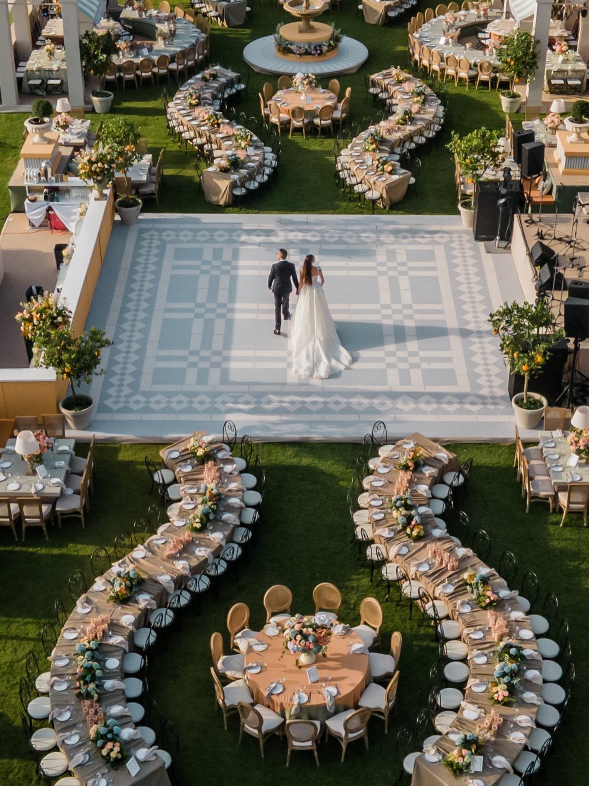 Bride and groom walking on a patterned dance floor surrounded by elegant wedding tables.