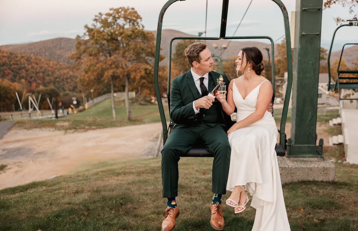 Bride and groom sitting on a ski lift chair with mountain views behind them.