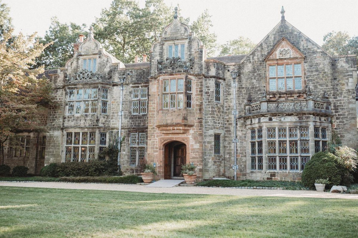 Historic stone manor house with ornate architecture and a green lawn in front.