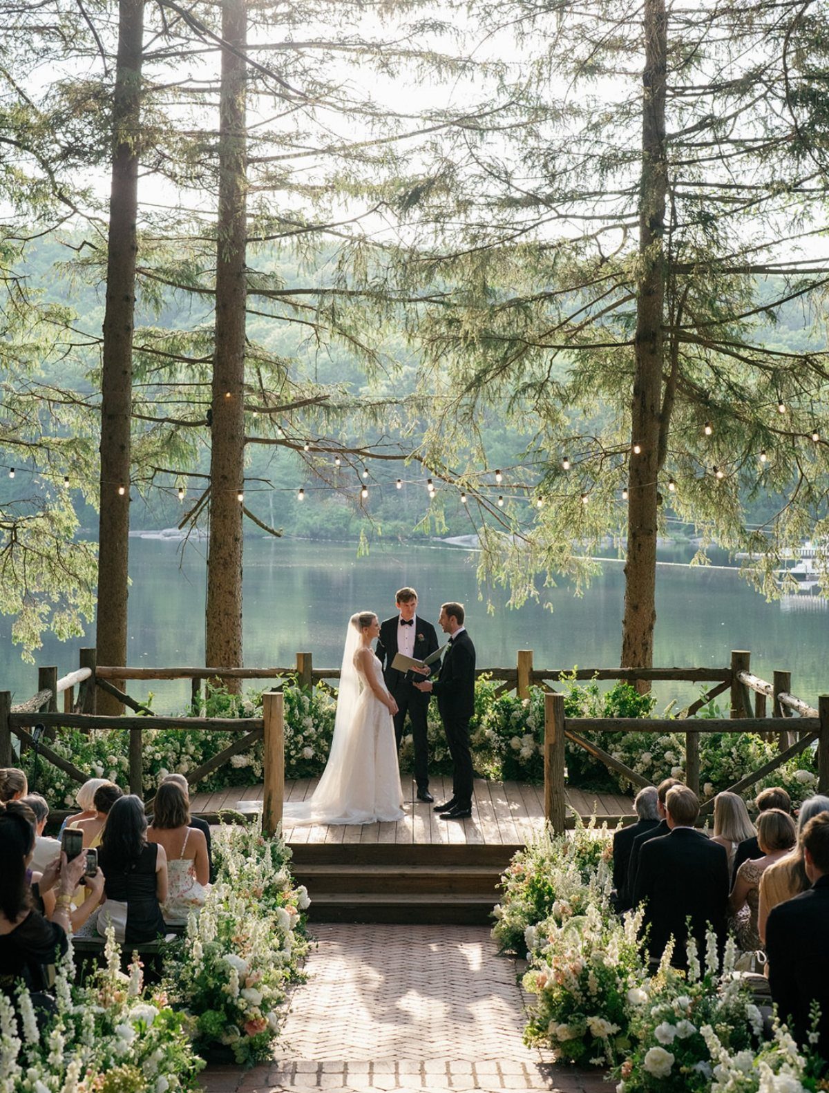 Wedding ceremony on a wooden deck overlooking a calm lake and green mountains.