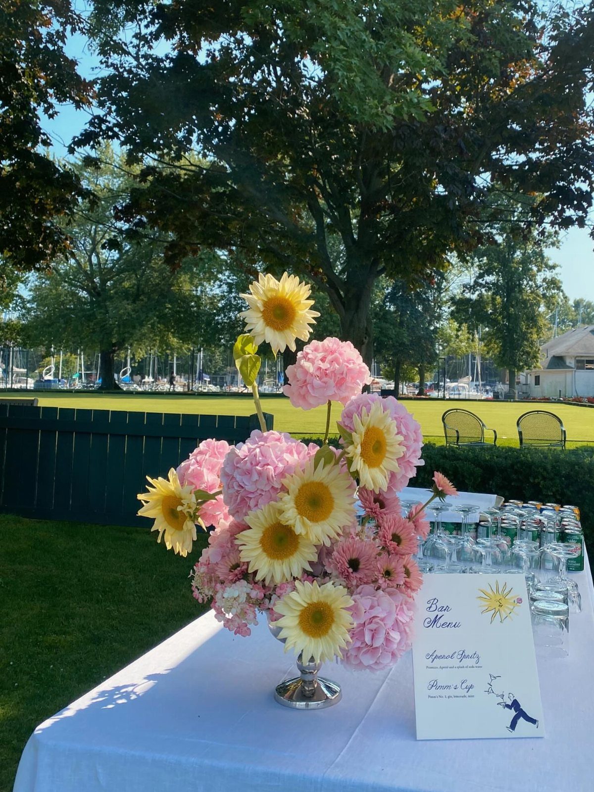 Floral arrangement of sunflowers and hydrangeas on a table overlooking a waterfront venue.