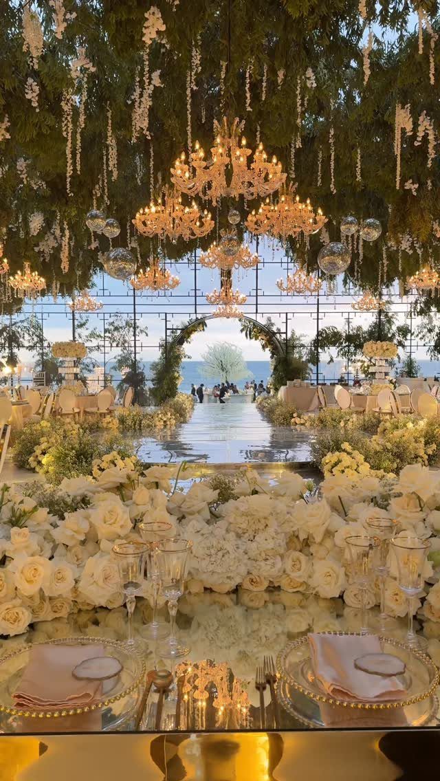 Opulent wedding reception with white flowers and chandeliers overlooking a calm blue sea.