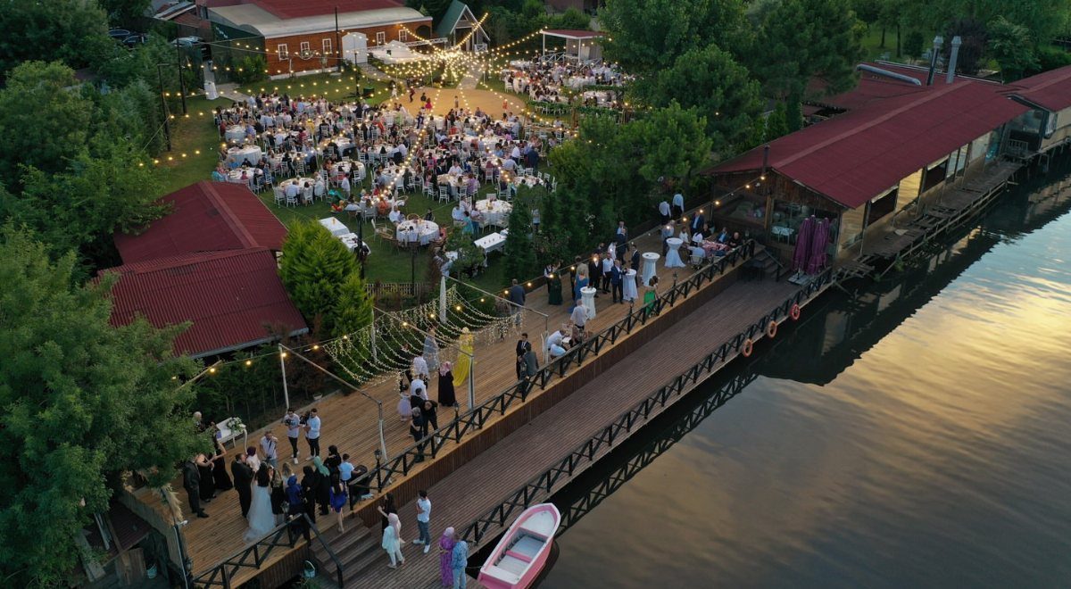 Outdoor wedding reception with guests on a lawn and pier beside a river