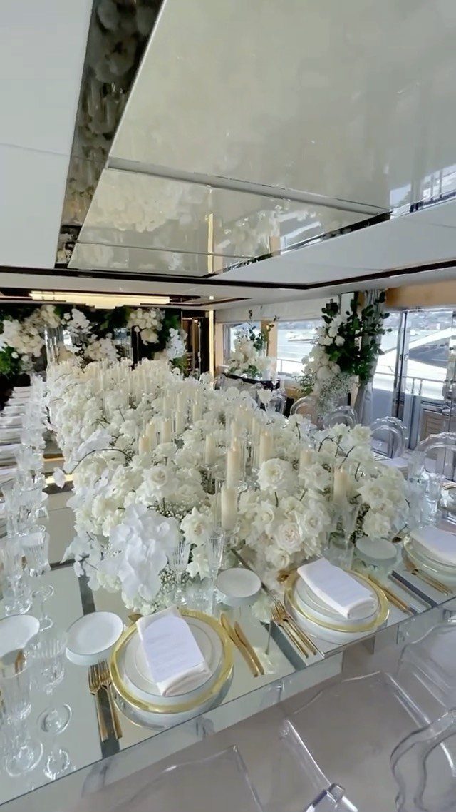 Wedding reception table with white flowers and gold plates inside a luxury yacht.
