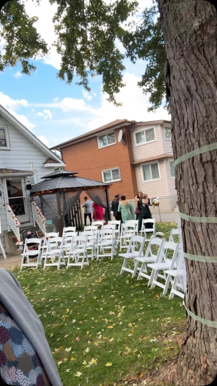 Backyard wedding ceremony setup with white folding chairs on a leaf-covered lawn.