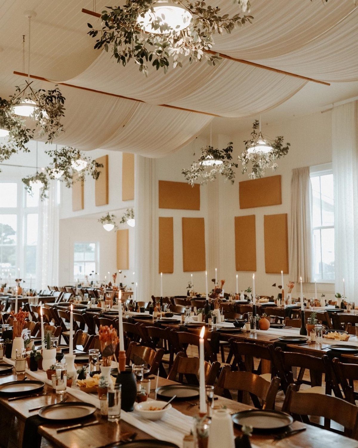 Long wooden dining tables with candles under a draped white fabric ceiling.