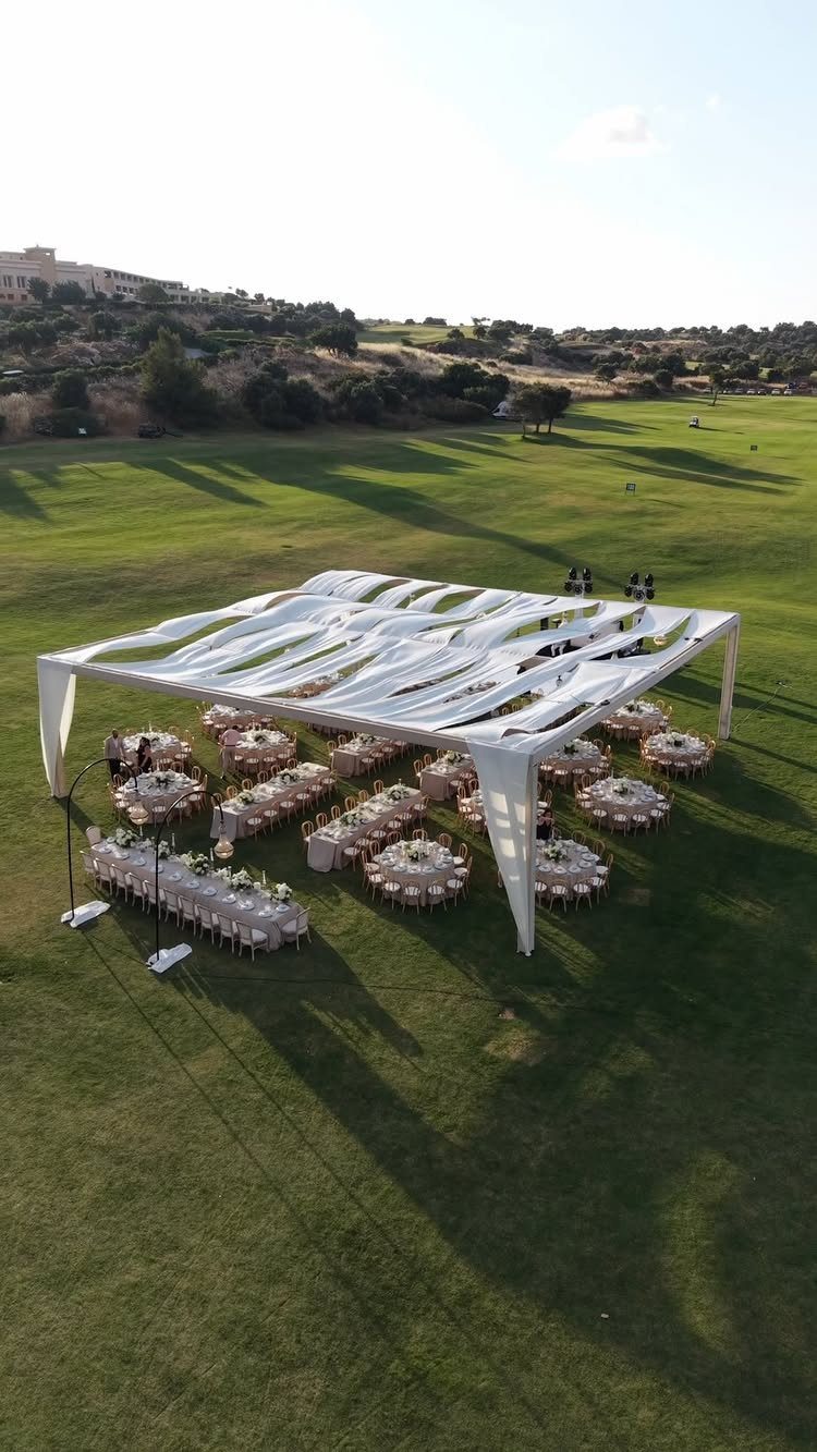 Outdoor wedding reception with white canopy and tables on a green golf course landscape