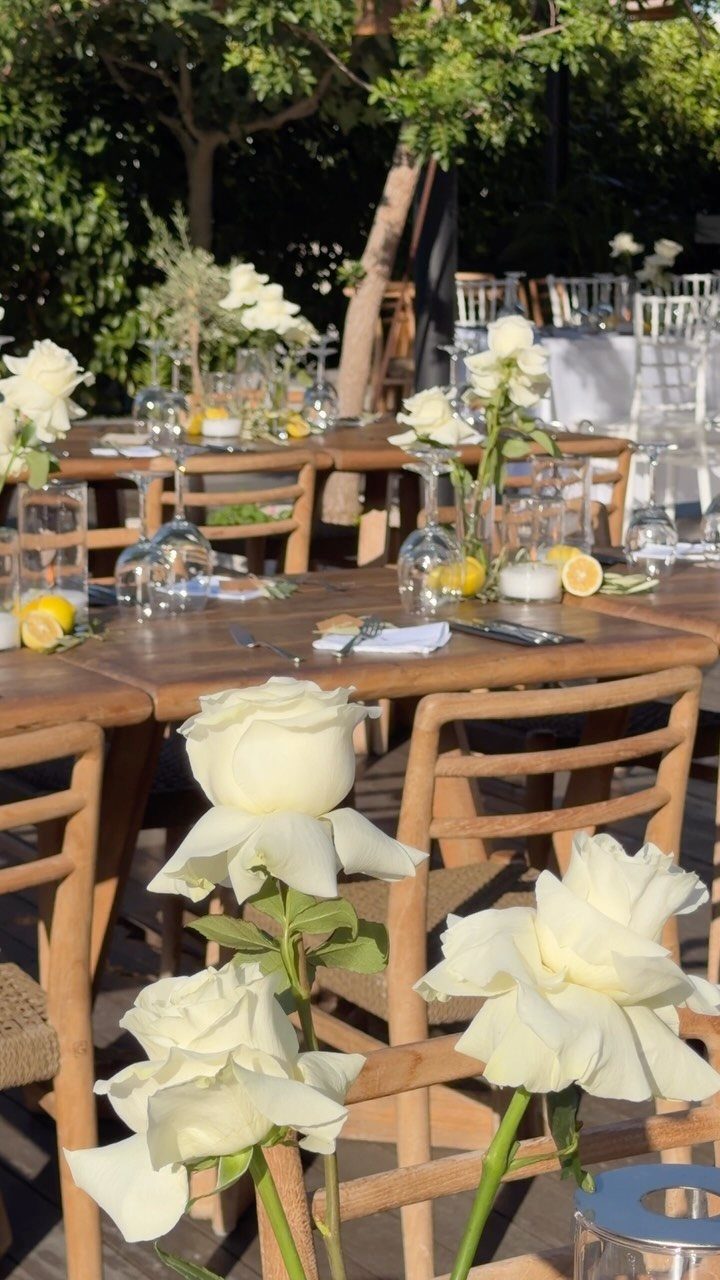Wooden outdoor dining tables decorated with white roses and lemons for a wedding.