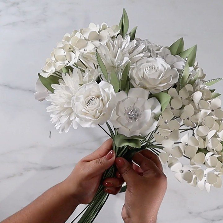 White foam flower bridal bouquet held by hands over a marble surface.