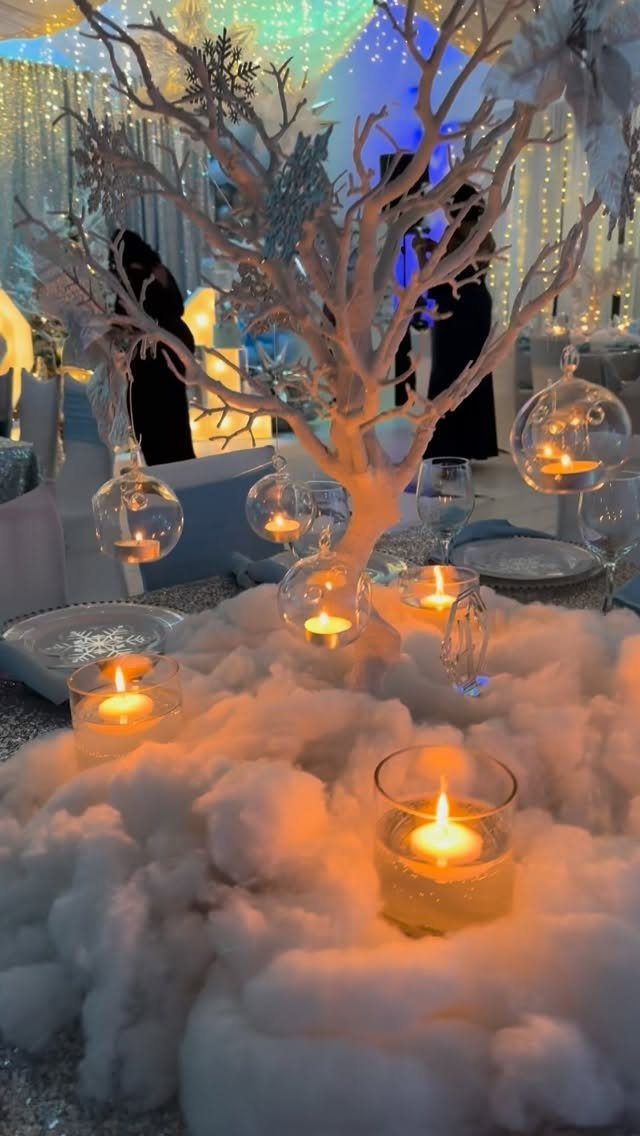 White artificial tree centerpiece with faux snow and glowing candles for winter wedding.