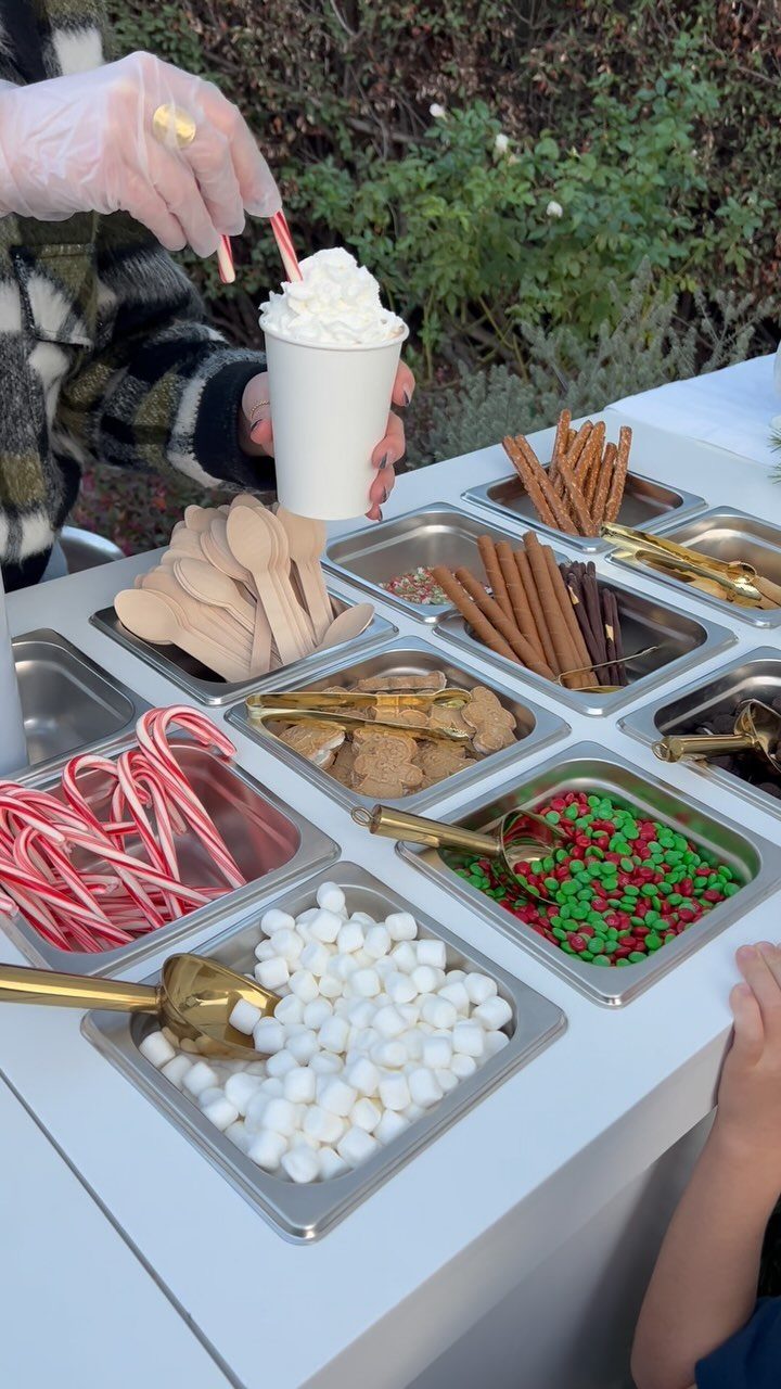 Hot cocoa bar with trays of marshmallows, candy canes, and cinnamon sticks.