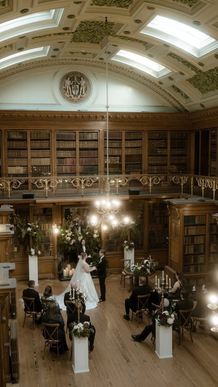 Wedding ceremony in a grand library with wooden bookshelves and a vaulted ceiling.