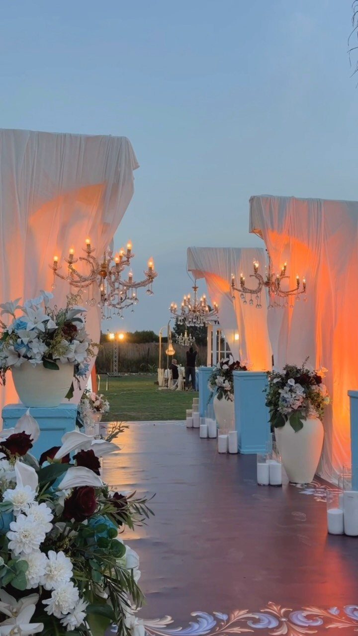 Wedding aisle with white fabric draping, gold chandeliers, and white floral arrangements.