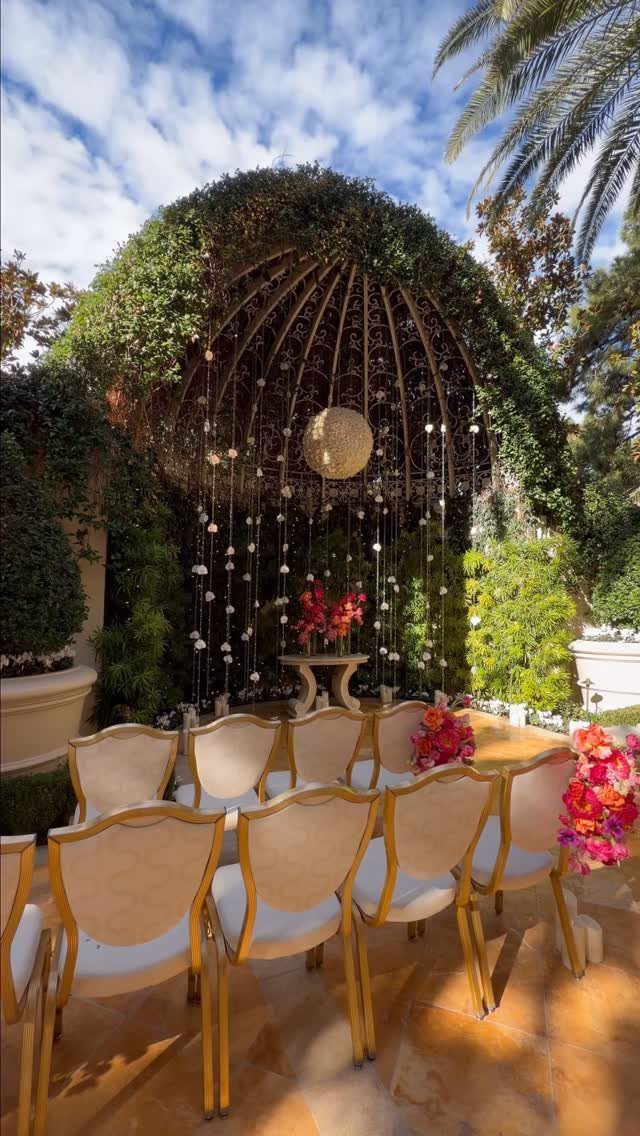 Outdoor wedding ceremony setup with gold chairs under a green leafy dome trellis.